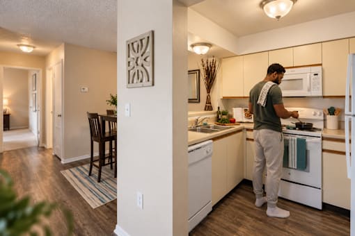 A man is standing in a kitchen with white appliances and wooden floors.