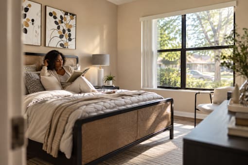 A woman is reading a book on a bed in a well-lit room.