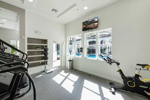 A gym with a treadmill, exercise bike and windows.