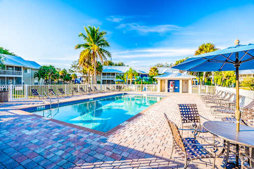 A pool surrounded by chairs and umbrellas with a building in the background.