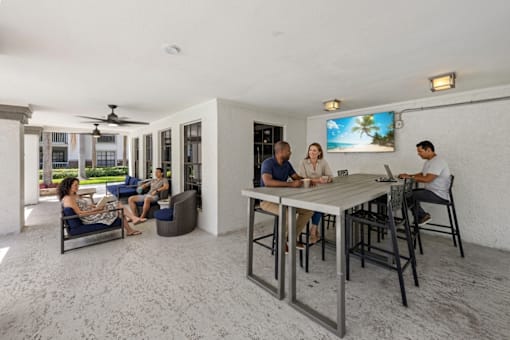 A group of people are sitting around a table in a room with a television.