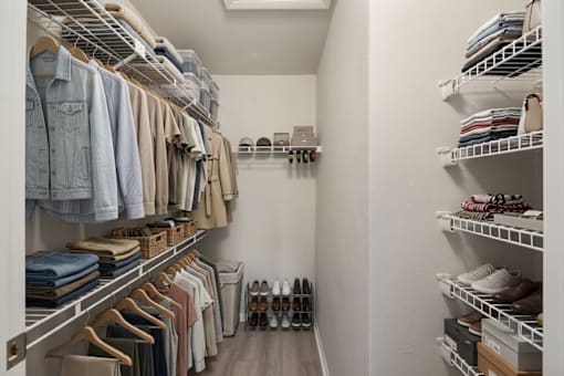A walk-in closet with clothes and shoes neatly organized on shelves and hangers.