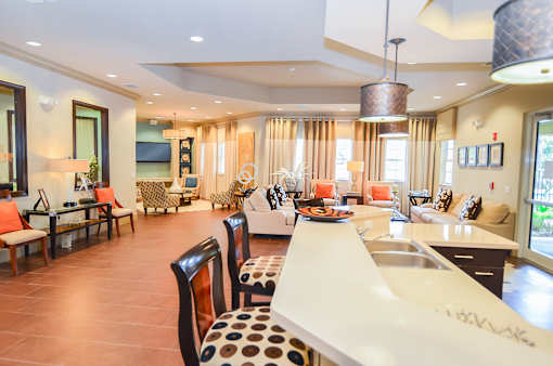 A modern kitchen with a long white island and brown chairs.