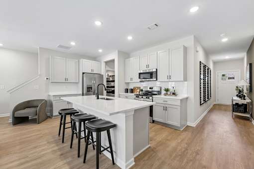A kitchen with white cabinets and a white island with three black stools.