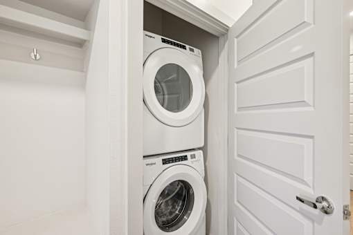 A white washing machine is in a cabinet under a white door.