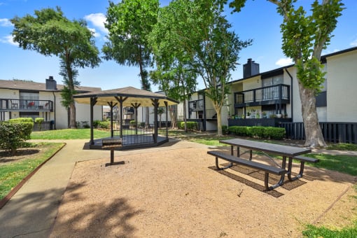 a picnic area with benches and trees in front of apartment buildings