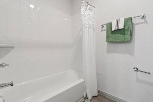 A white bathroom with a white tub and a green towel hanging on the towel rack.