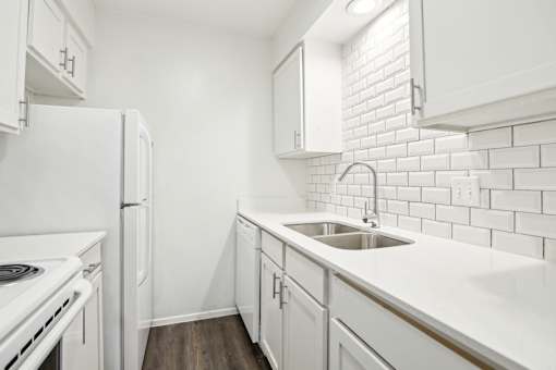 A white kitchen with a white fridge and white cabinets.