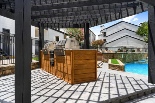 an outdoor barbecue area with a pool in the background and a pergola in the foreground