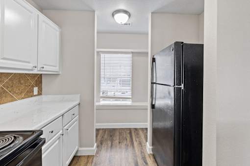 A kitchen with a black fridge, white cabinets and a stove top.