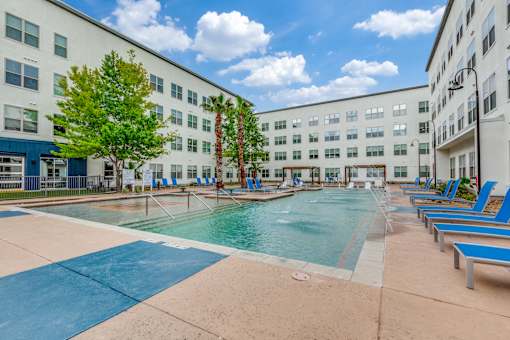 A large swimming pool surrounded by blue lounge chairs and palm trees.