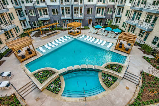 A large outdoor swimming pool surrounded by a patio area with chairs and umbrellas.
