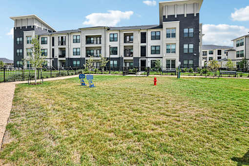 A large grassy area in front of apartment buildings with a red fire hydrant and a blue playground.