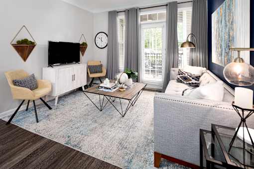 A living room with a grey sofa, a wooden chair, a white cabinet, a TV, a clock, and a rug.