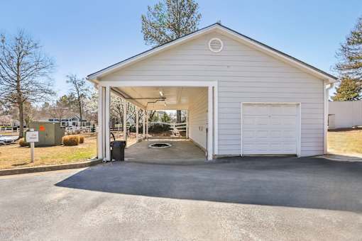 A white garage with a door open and a trash can in front.