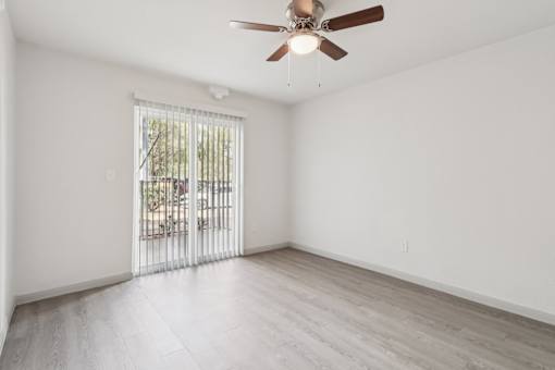 A room with a ceiling fan and sliding glass doors leading to a balcony.