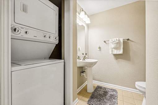 A white washing machine is in a bathroom next to a white sink.