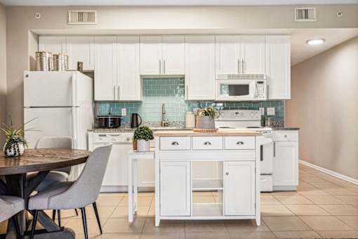 A kitchen with white cabinets and appliances, a table with chairs, and a plant on the counter.