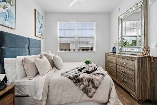A bedroom with a large bed, a wooden dresser, and a window with blinds.