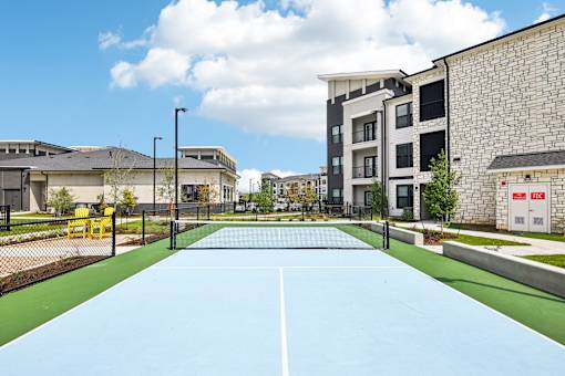 A tennis court is surrounded by apartment buildings.
