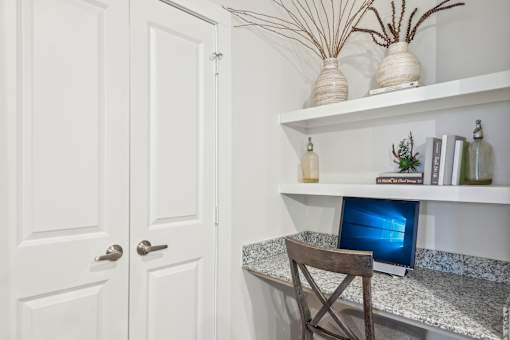 A white door is on the left and a desk with a laptop on it is on the right.