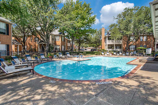 A pool surrounded by trees and chairs in a sunny day.
