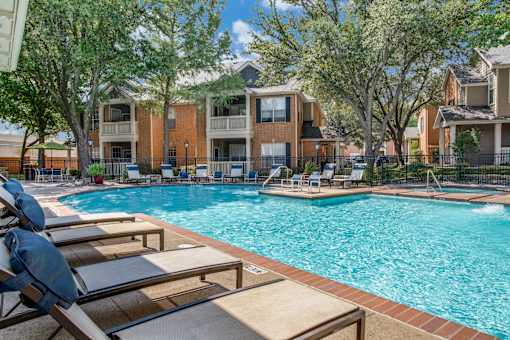 A pool surrounded by lounge chairs and trees.