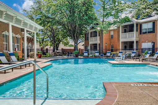 A swimming pool in front of a building with a white pergola.