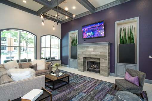 A living room with a grey couch, a coffee table, a fireplace, and a flat screen TV mounted on the wall.