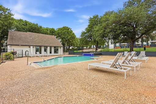 A pool surrounded by chairs and trees with a building in the background.