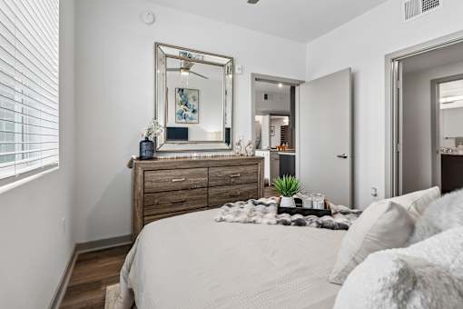 A bedroom with a large bed, a wooden dresser, and a mirror above it.