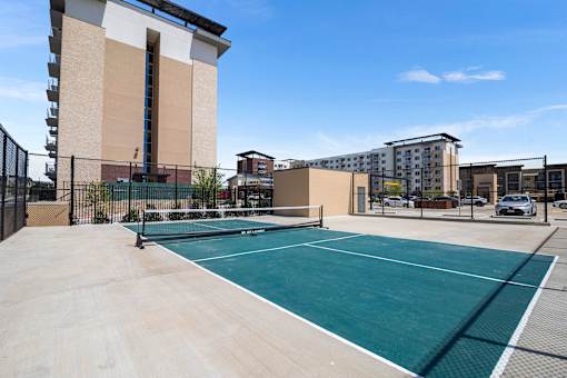 A tennis court is surrounded by a fence and a building.