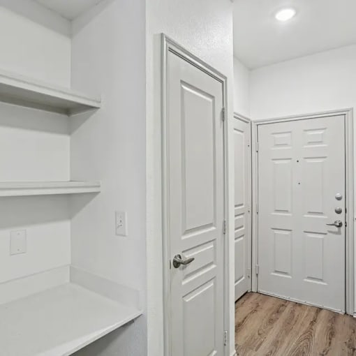 A white door is in a white room with a shelf to the left.