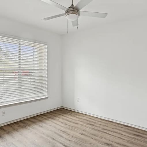 A room with a ceiling fan and a window with blinds.