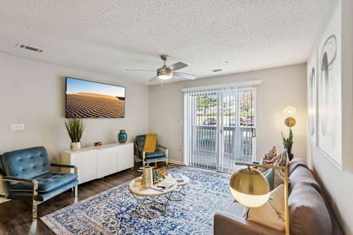 A living room with a blue rug and a painting of a desert on the wall.