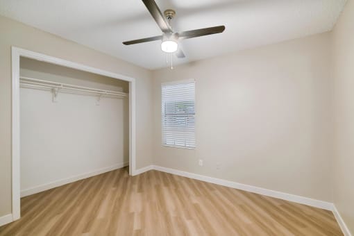 an empty bedroom with a ceiling fan and a closet with a window