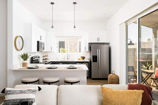 A modern kitchen with a breakfast bar and a white couch with pillows.