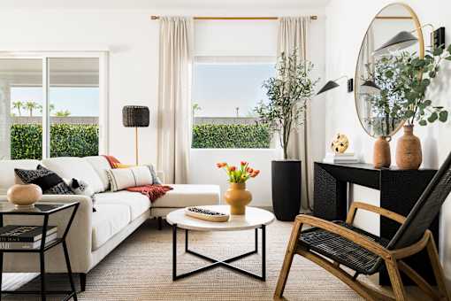 A living room with a white sofa, a coffee table, a chair, and a round mirror.