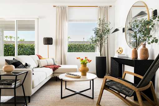 A living room with a white sofa, a coffee table, a chair, and a round mirror on the wall.
