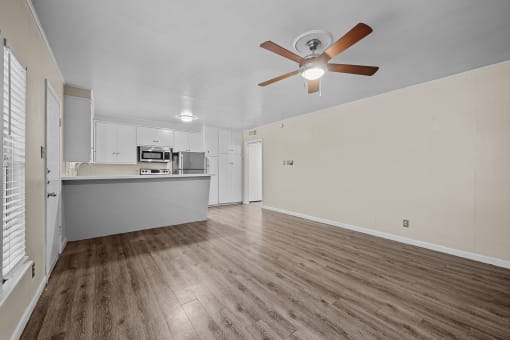 an empty living room with a ceiling fan and a kitchen
