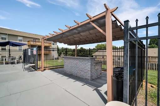 A patio with a black fence and a brick wall under a wooden pergola.
