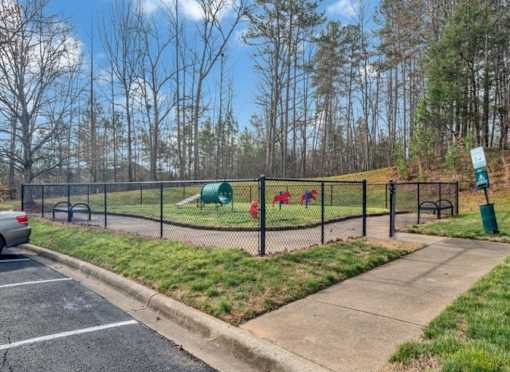 A playground with a green slide and red swings is enclosed by a black fence.