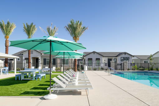 a pool with lounge chairs and umbrellas in front of a house