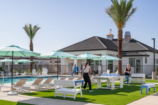 a group of people walking around a pool and patio with tables and umbrellas