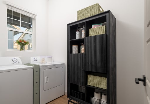 a utility room with a washer and dryer and a black shelf with baskets