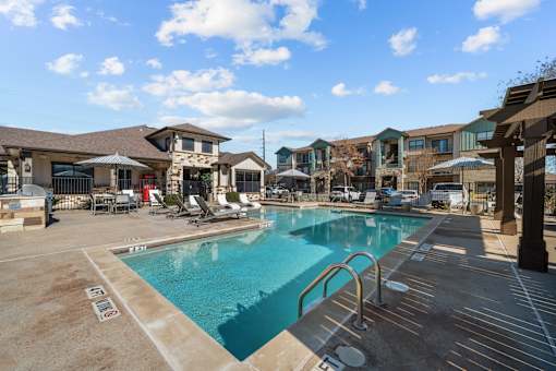 A large swimming pool surrounded by a patio area with chairs and umbrellas.
