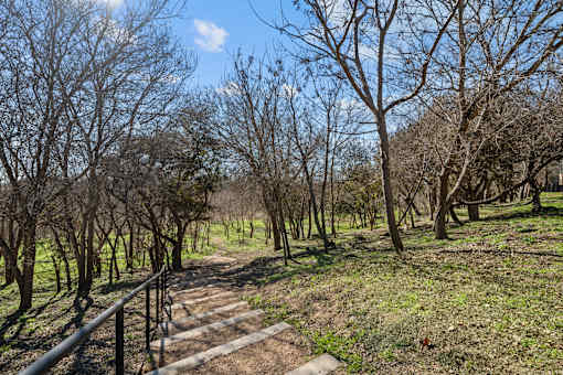A pathway with a metal railing on the left side leads through a grassy area with trees on both sides.