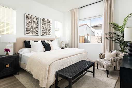 A bedroom with a large bed, a chair, and a potted plant.