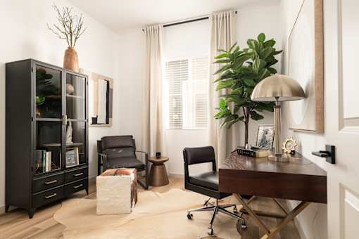 A black bookcase with a chair and a table with a lamp.