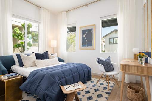 A bedroom with a bed covered in a blue comforter and a white chair.